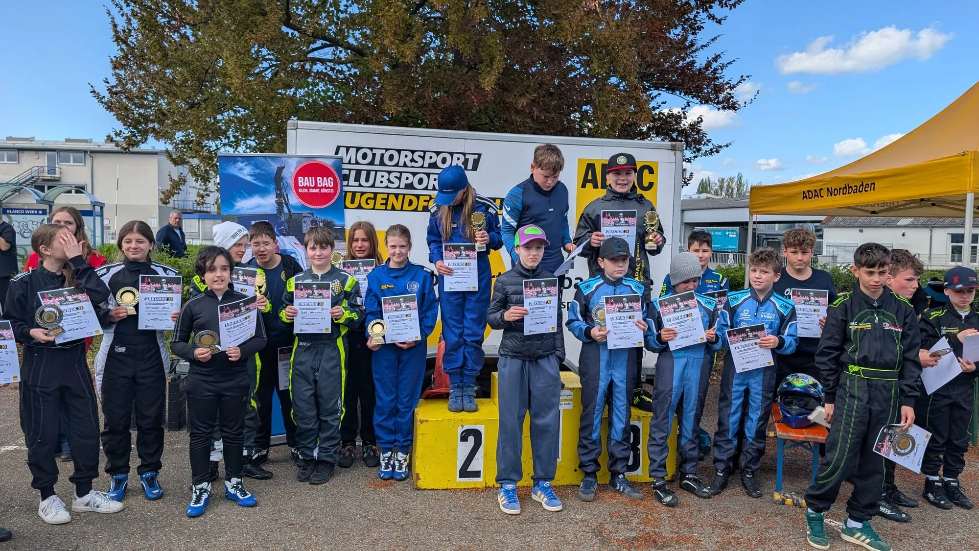 Siegerehrung beim Jugendkartslalom, Kinder in Rennanzügen mit Urkunden vor dem Podest
