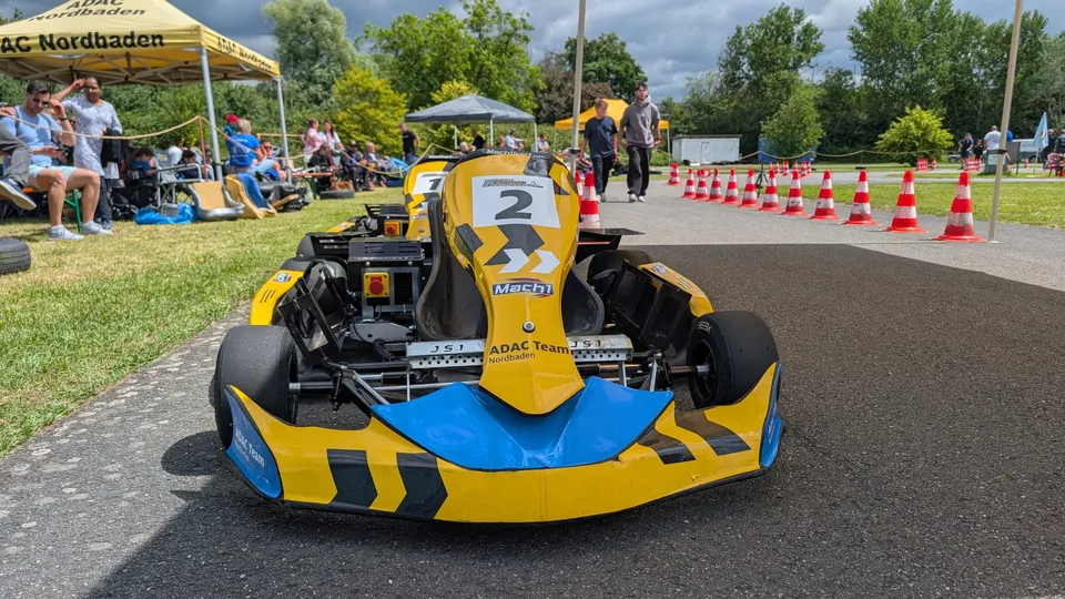 Elektrokart mit Startnummer 2 an der Startlinie, Zuschauer unter Zelten am Rand