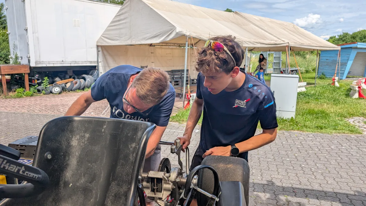 Zwei Vereinsmitglieder arbeiten gemeinsam am aufgebockten Kart.