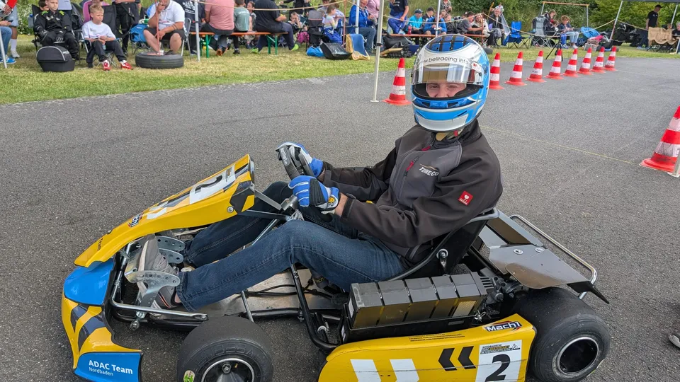 Nachwuchsfahrer im gelben Elektrokart mit Startnummer 2 im Parcours, Zuschauer am Rand