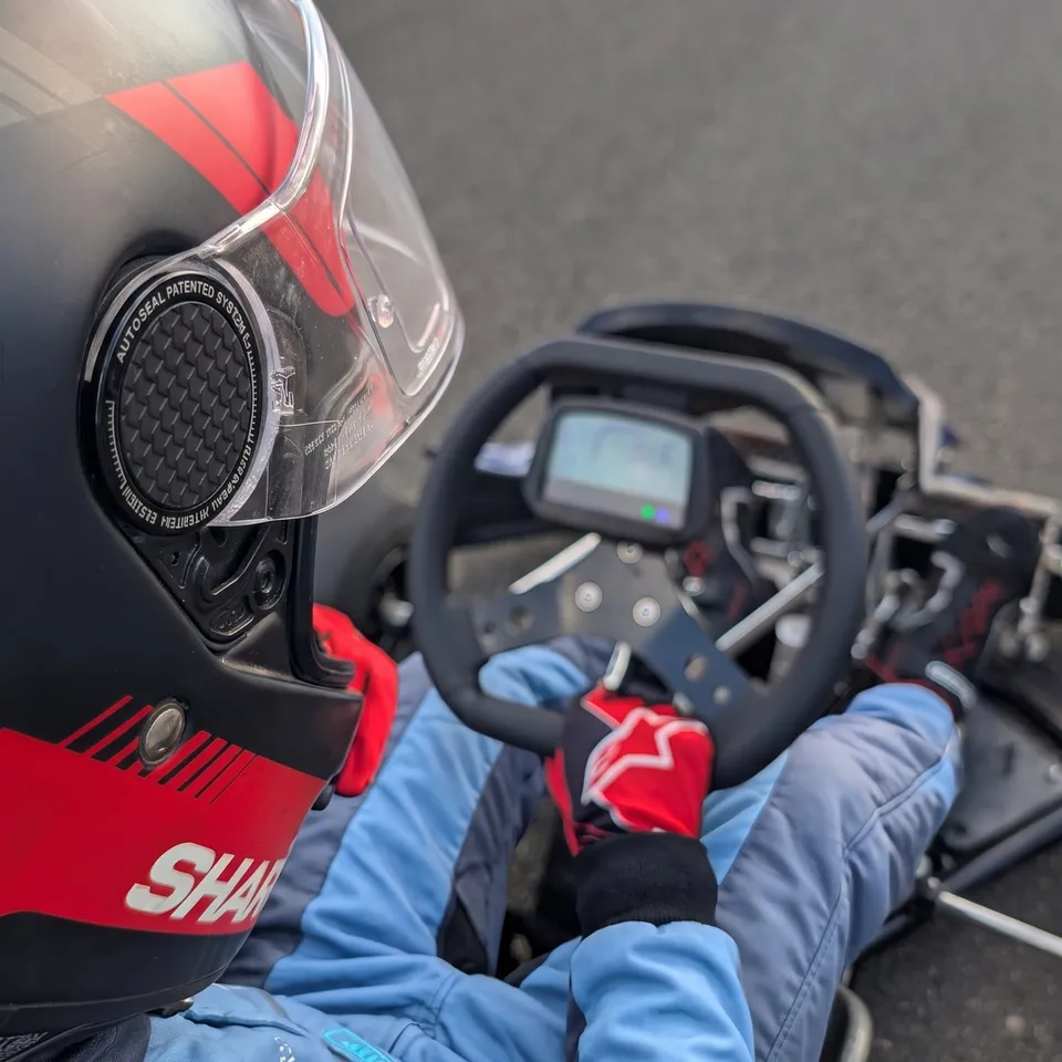 Blick über die Schulter eines Fahrers mit rot-schwarzem Helm auf Lenkrad und Display