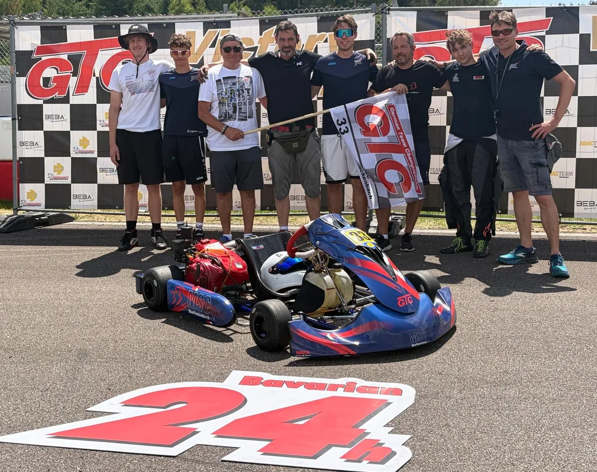 Das Team der Nummer 33 mit seinem blauen Kart vor der Victory-Lane-Wand