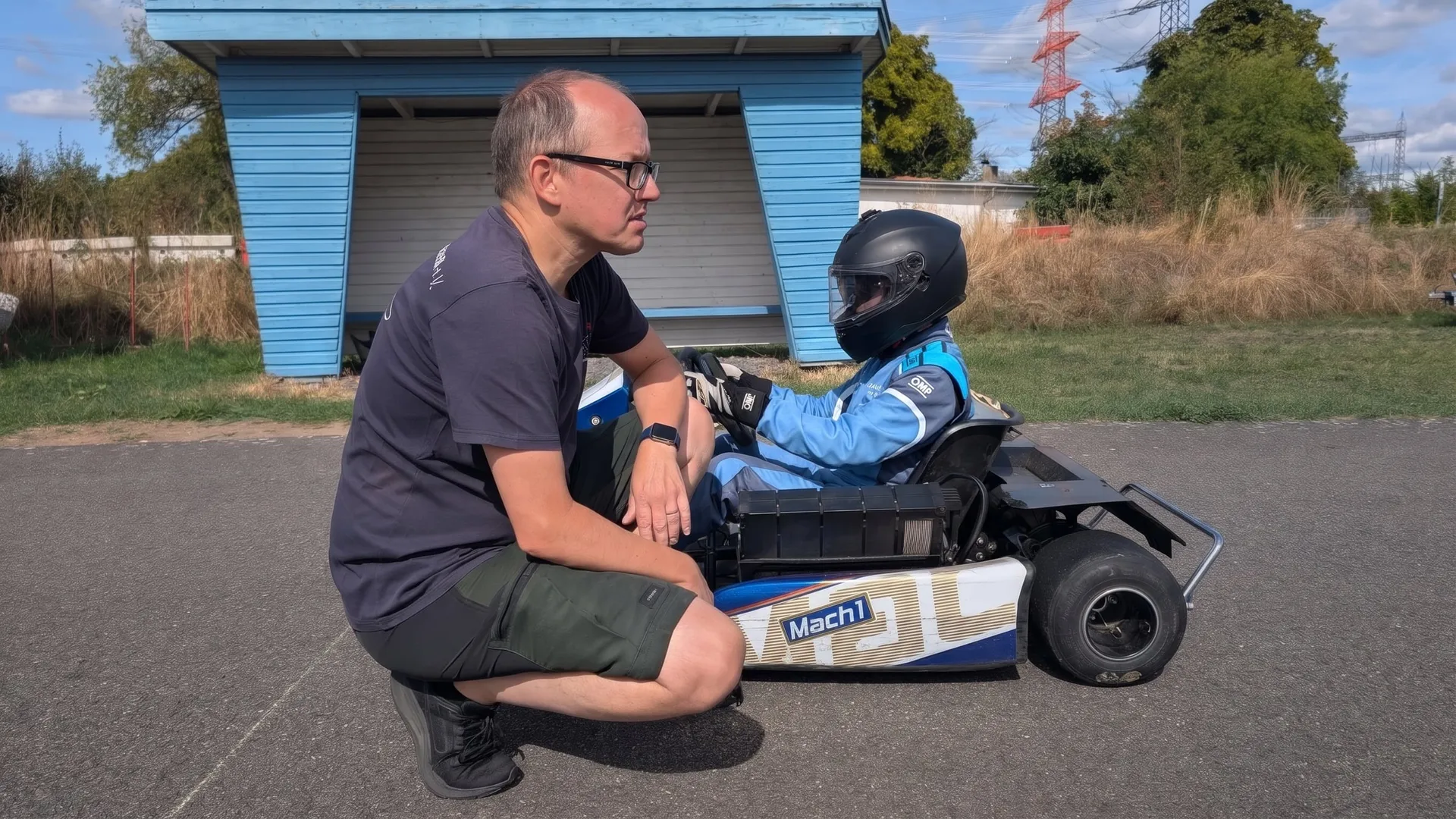 Ein Trainer kniet neben dem Vereinskart und bespricht mit dem Nachwuchsfahrer im Rennanzug den nächsten Durchgang
