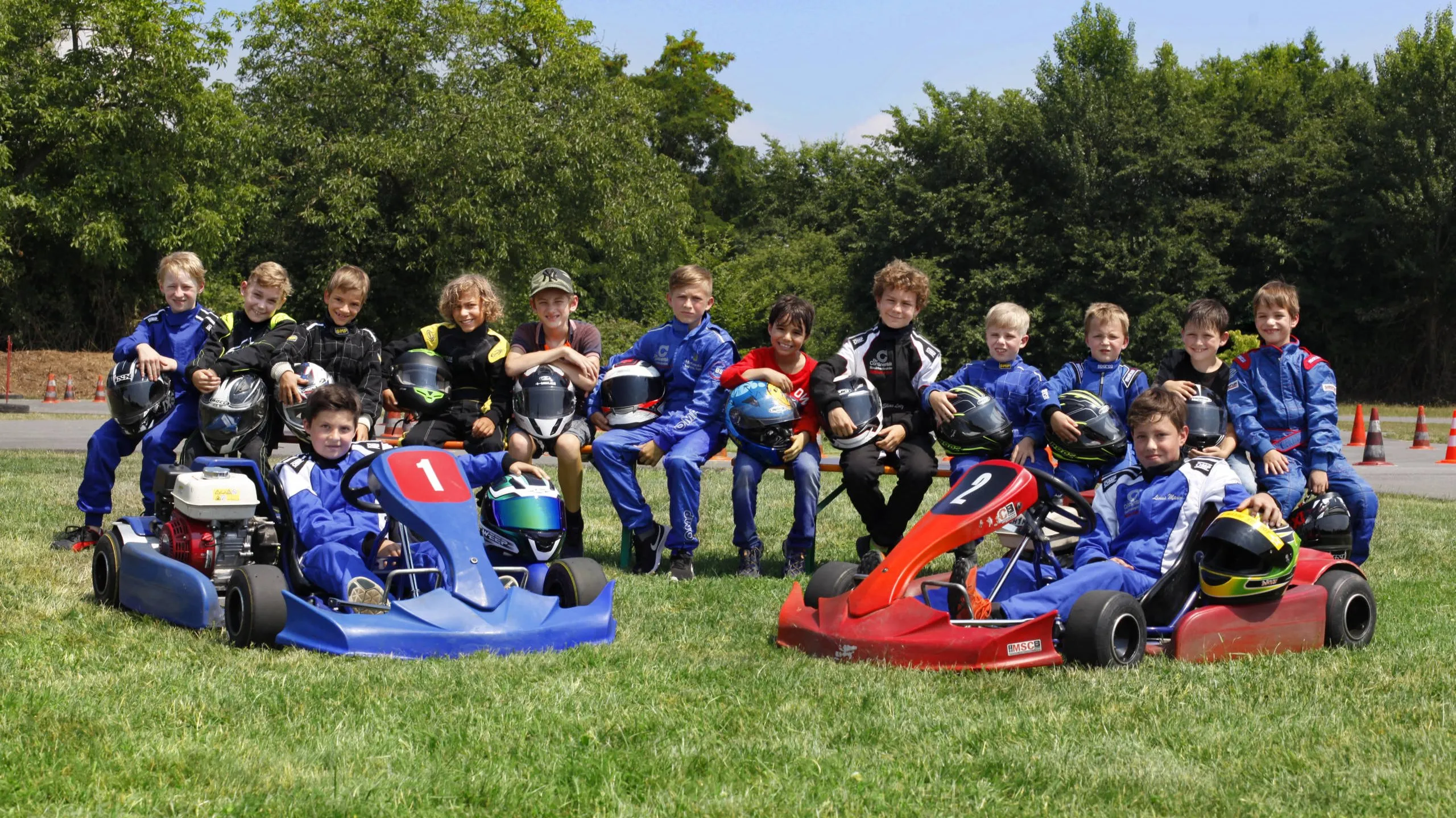 Gruppe von Kindern und Jugendlichen in Rennanzügen mit Helmen, dahinter zwei Slalomkarts auf dem Vereinsgelände.